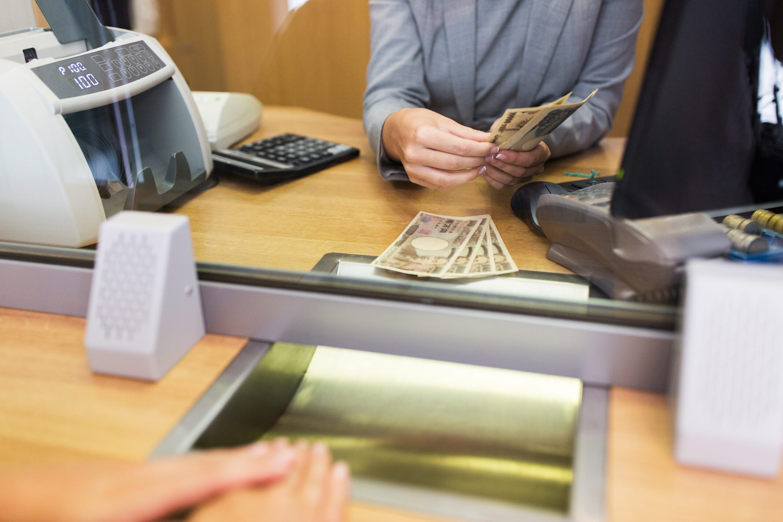 Bank teller counting cash in front of a customer at the bank office.